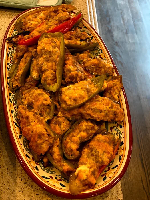 Platter of stuffed jalapeño peppers filled with a savory mixture, garnished with red chili peppers, served on a decorative dish, ideal for appetizers or party snacks.