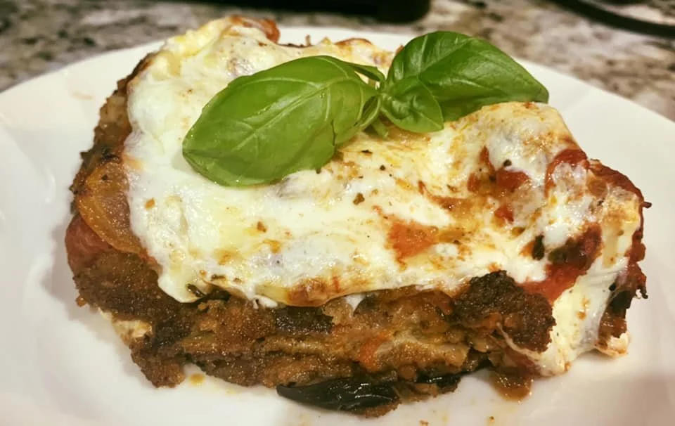 Delicious homemade eggplant parmesan slice topped with melted cheese and fresh basil, served on a white plate.