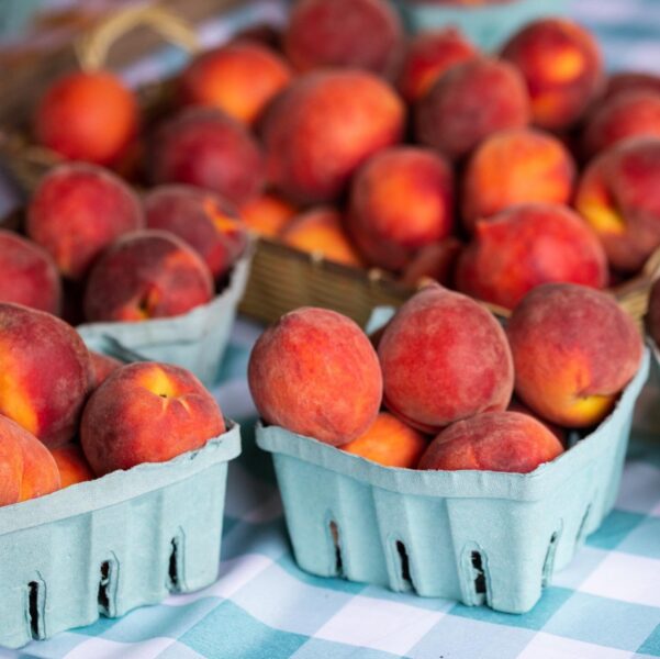 Fresh, ripe peaches in blue berry baskets at a farmer's market, showcasing a vibrant assortment of orange and red fruits on a checkered tablecloth.