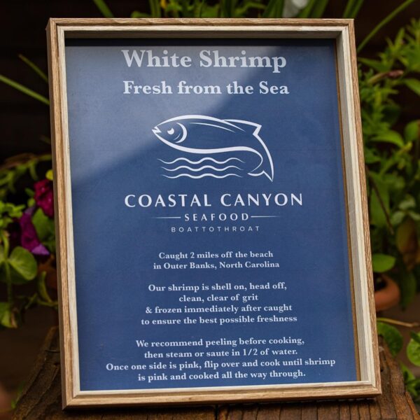Informative sign for Coastal Canyon Seafood featuring white shrimp caught off the coast of Outer Banks, North Carolina. The sign details preparation recommendations, including peeling, steaming, or sautéing for optimal freshness and cooking instructions.